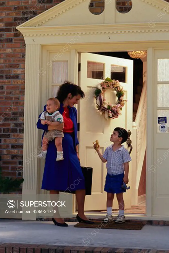 Working mother at the front door with her two children.  (model released)
