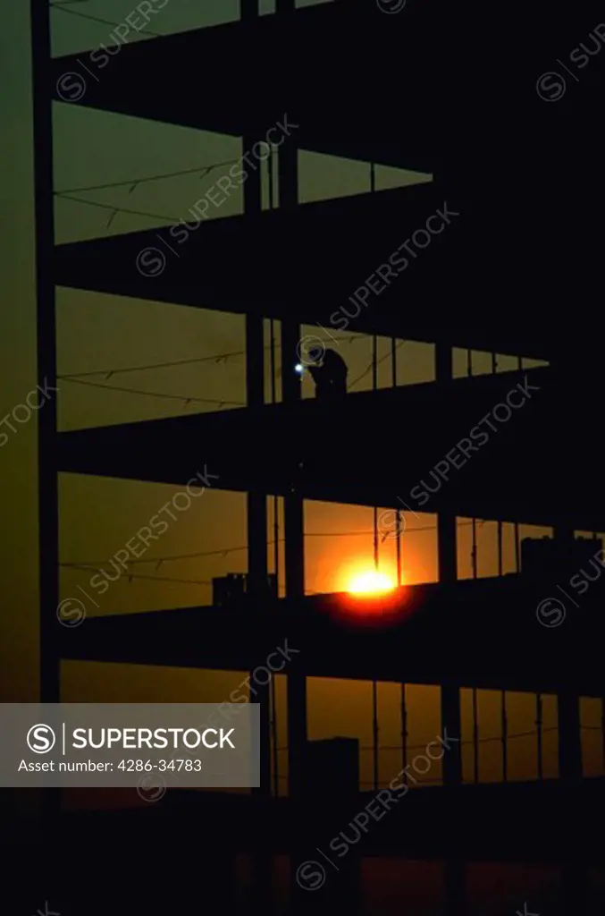 Construction worker does welding on a high rise building at sunrise