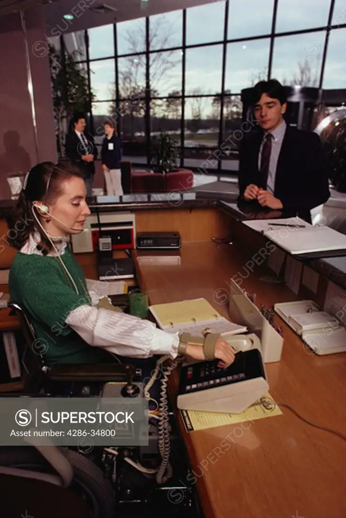 Receptionist with physical handicap greets people at corporation in Virginia.