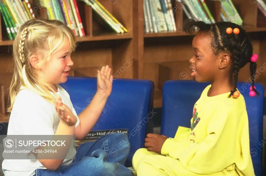Female first grade students talking in library.  (model released)