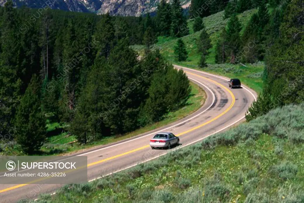 Cars on highway curving into the Grand Teton Mountains.