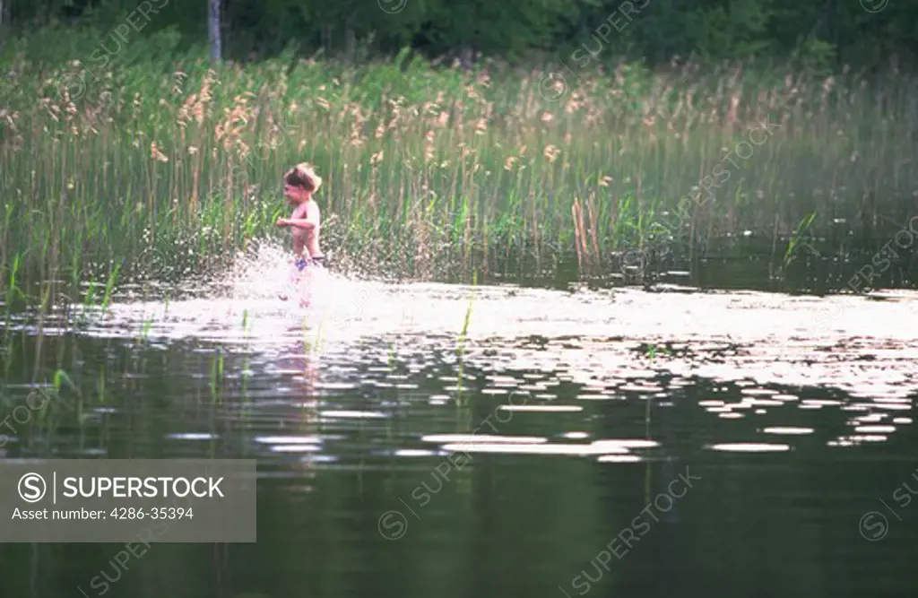 Young boy running through the water along a lake in Southern Finland.