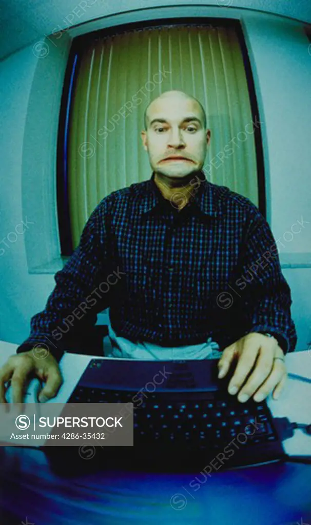 Bald man with a very stressed look on his face using a laptop computer in the office.