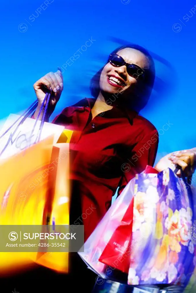 A smiling African American woman wearing sunglasses carrying shopping bags.
