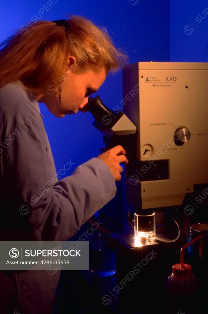Research technician using microscope in product testing laboratory.