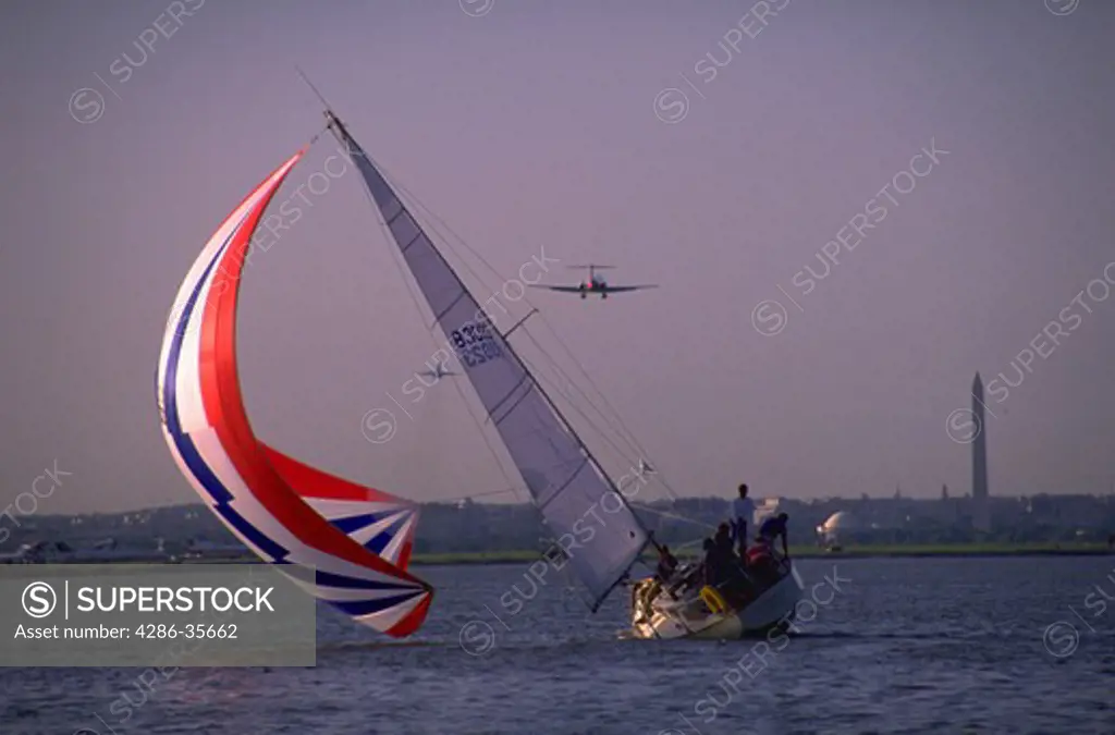 Sailing on the Potomac River in the Nations capital.  Washington, DCs Washington Monument is prominent in the background.  Sailboat showing lots of action - extreme angle.  Background with airplane in sky, near Washington National Airport.  (Washington, DC.  Recreation.  Boating.  Aviation.)