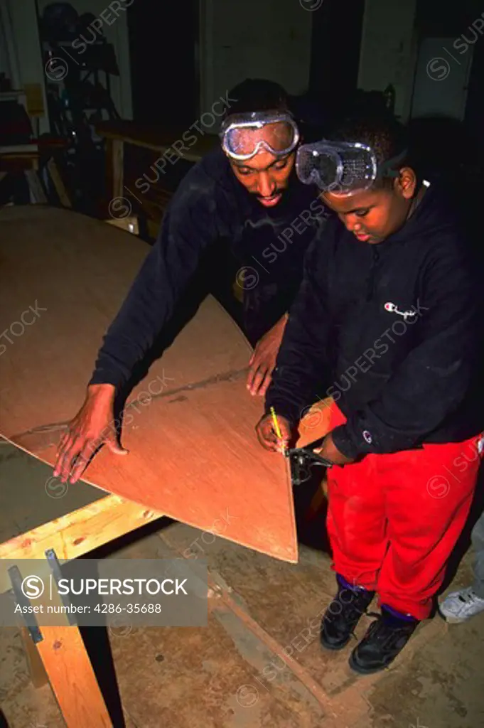 Black man teaching black boy how to use tools.  Taking social responsibility.  Providing guidance and serving as a role model. Making a difference and getting involved.  Shot taken at the Alexandria Seaport Foundations Boatbuilding School, where disadvantaged youths, and anyone in the community, can receive instruction and use facilities to build traditional wooden boats and other related projects.  Located in Alexandria, Virginia.  The adult is Mr. James Moore and the youth is Cory Braxton.  F