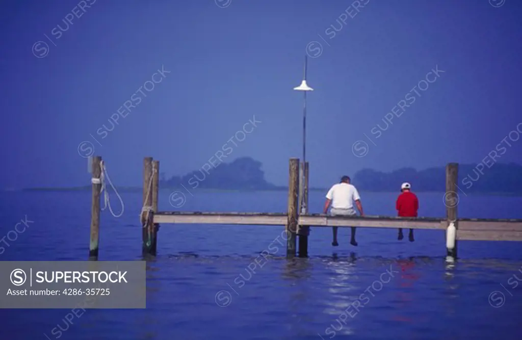 Man and boy (father and son) sitting on a dock, on Rehoboth Bay, Delaware.