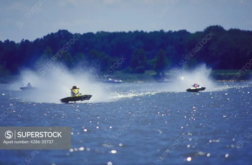 Hydroplane boats, racing.  Waterspray is flying as the boats come blazing down the front straightway on the racecourse during a professional powerboat race. 