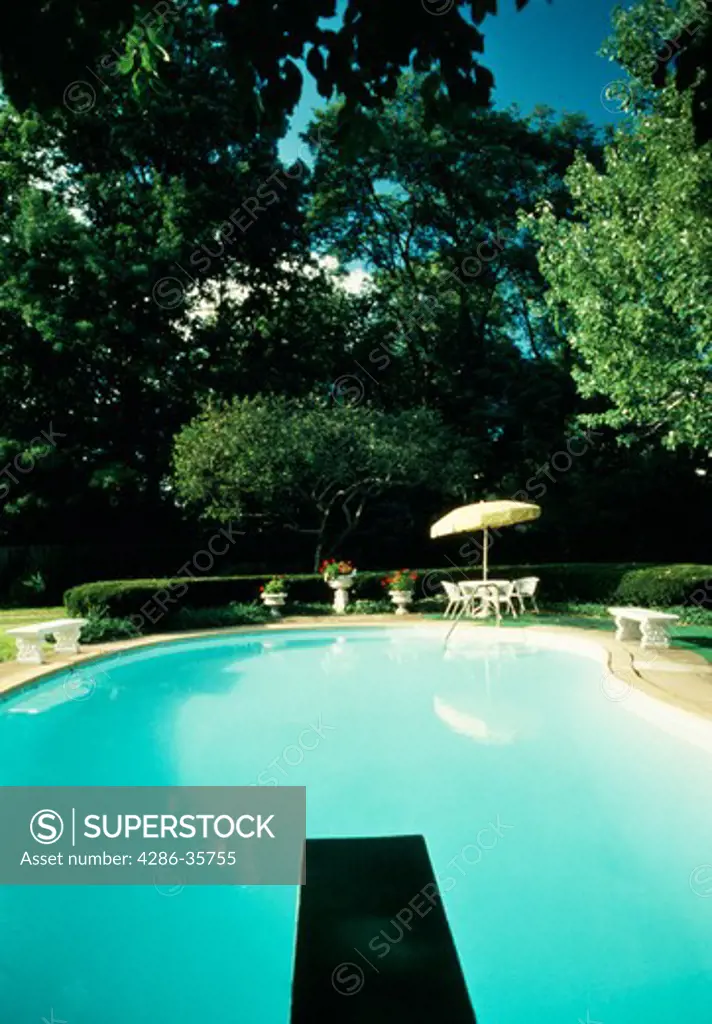 Swimming pool with diving board at private residence.  Picnic table and umbrella visible in background of yard shaded with trees.  (Leisure.  Water.  Recreation.  Good Life.)