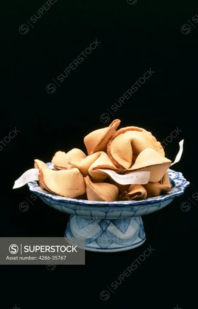 Fortune cookies in a blue and white oriental style bowl.  Some paper 'fortunes' are visible.  Other variations available. (Concept. Still Life.)