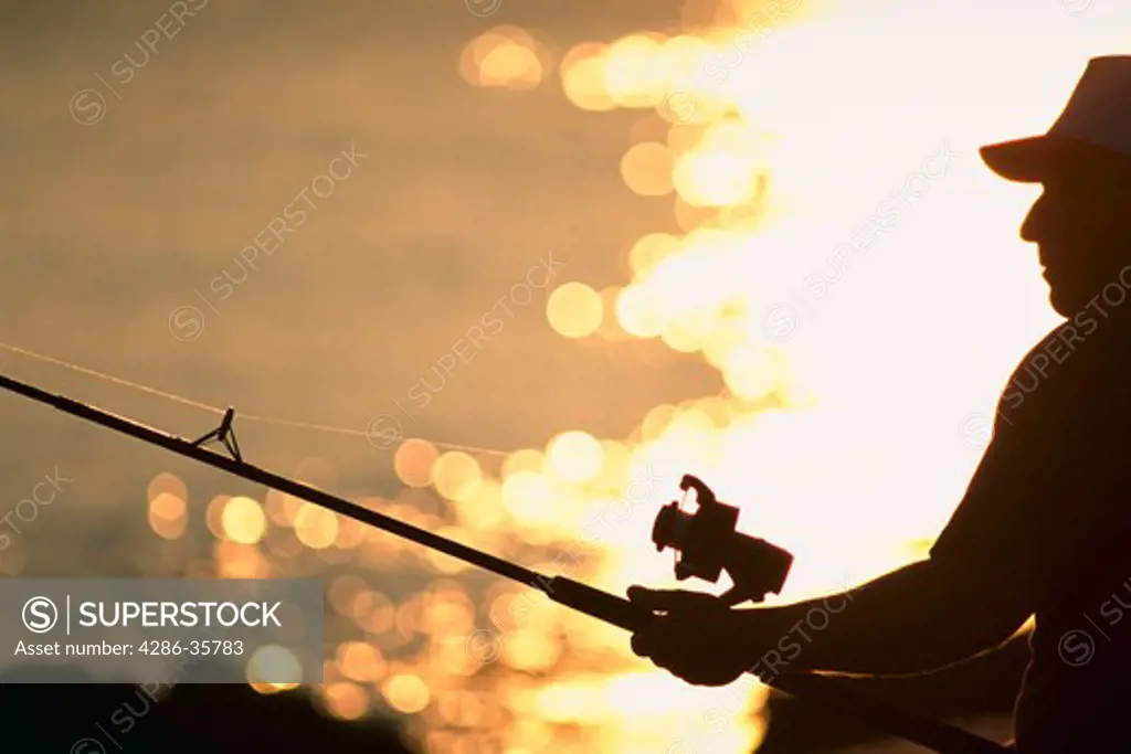 Man fishing, backlit with glistening water.  large fishing and boating file available. (Recreation. Fishing. People. Concept.)