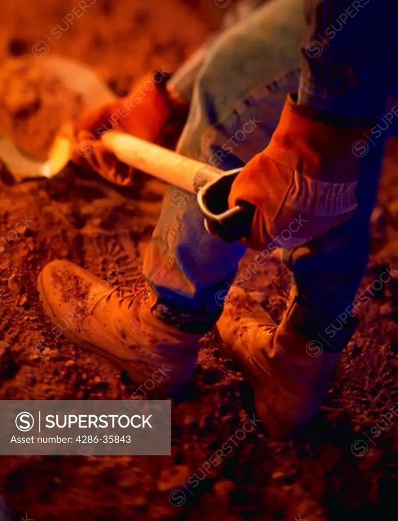 Man with work boots and leather work gloves shoveling dirt.