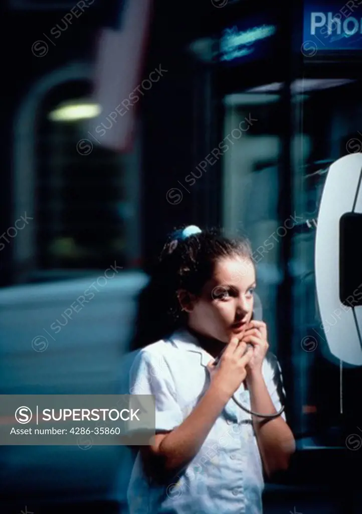 Young girl talking on public pay phone at night.