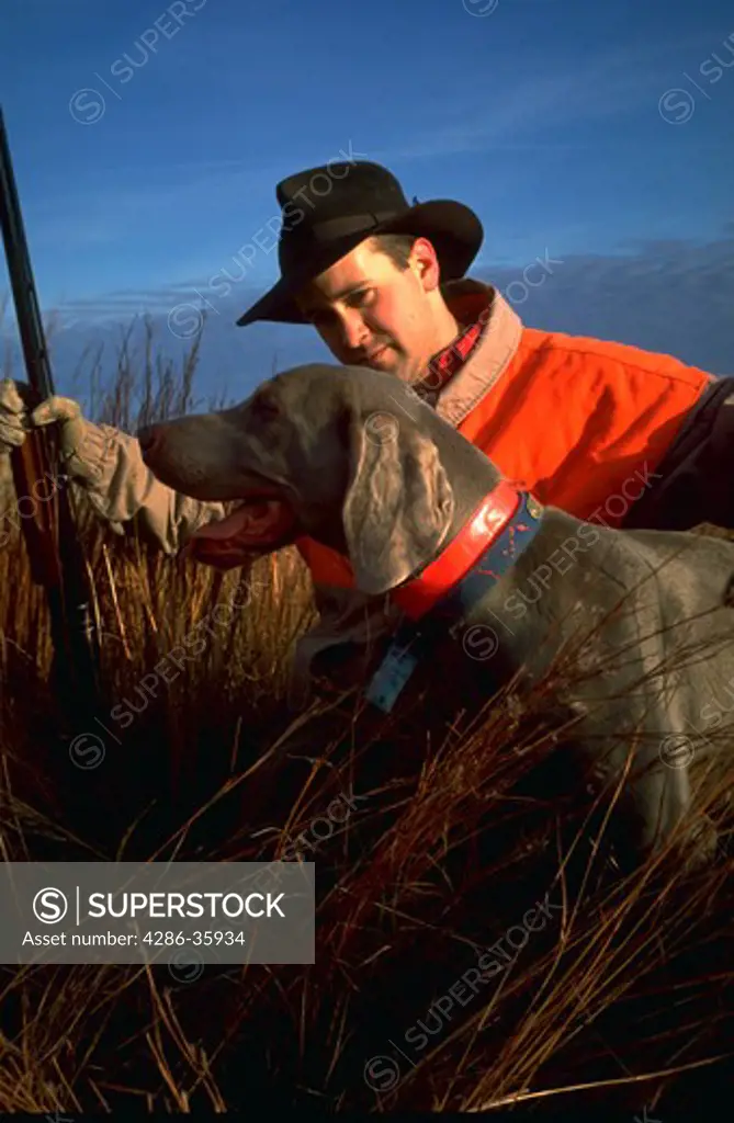 Pheasant hunter sitting in tall grass with his dog near Utica, Ness County, Kansas.