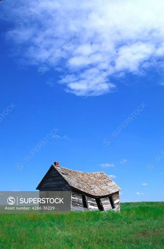Abandoned one-room schoolhouse with sagging walls and roof on the eastern prairies of Colorado on a bright spring day.