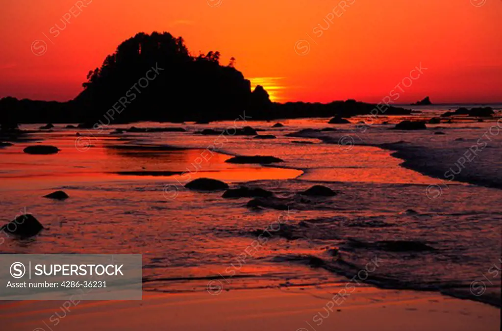Waves rolling into shore against orange sky at sunset on Ozette Indian Reservation, contiguous to Olympic National Park, Washington.