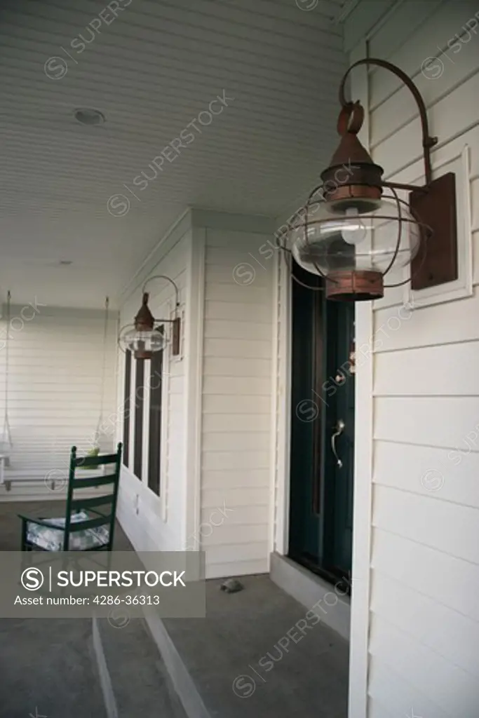 Still view of a rocking chair on the front porch of a home and close-up of the porch lamps. 