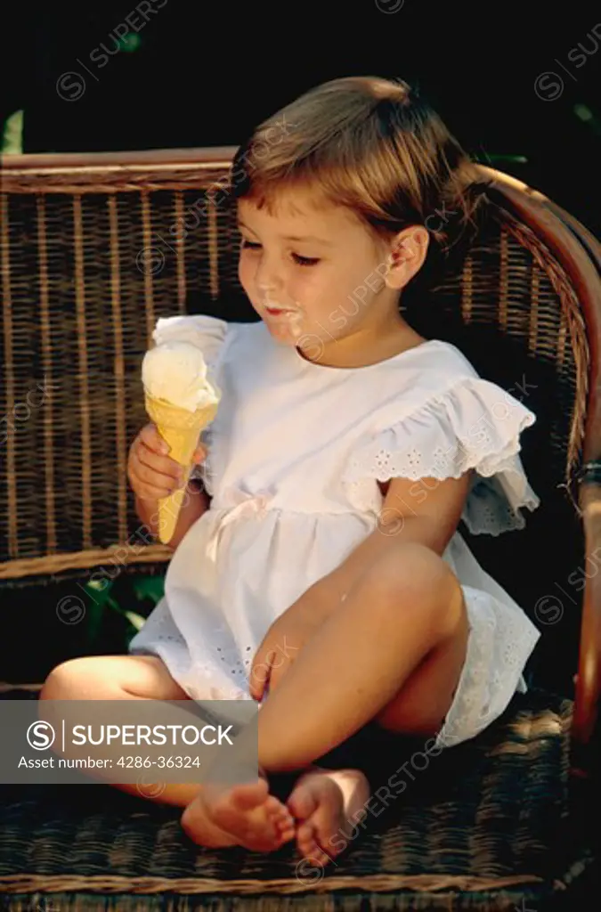 Toddler girl sitting on an outdoor bench eating an ice cream cone. 