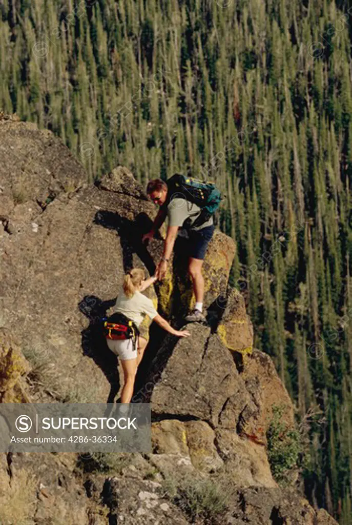 Man and woman couple hiking up a rocky hill side terrain high above the tree tops in Idaho.