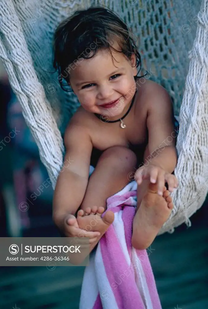 Young girl sitting in a hammock with a beach towel around her feet smiling towards the camera. 