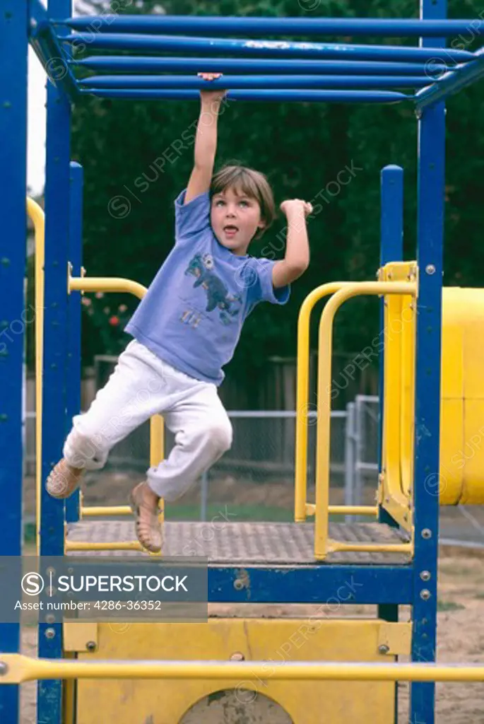 Young girl playing outside specifically swinging on monkey bars. 
