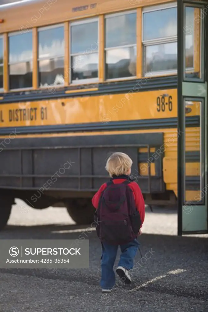 Little blond hair boy wearing his backpack getting ready to climb on to a school bus. 