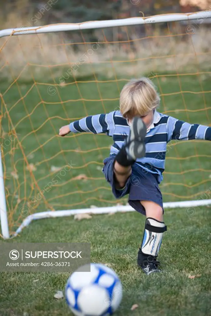 Little blond boy  kicking  a soccer ball with all his might in front of the goal. 