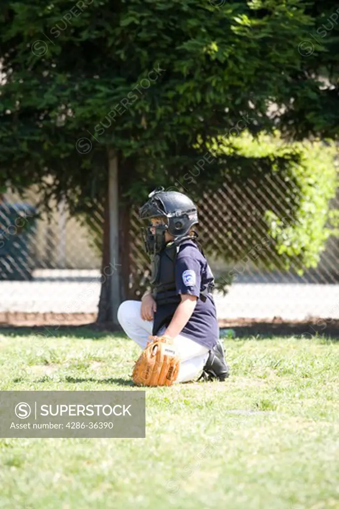 Young boy playing youth league baseball, catcher squatting