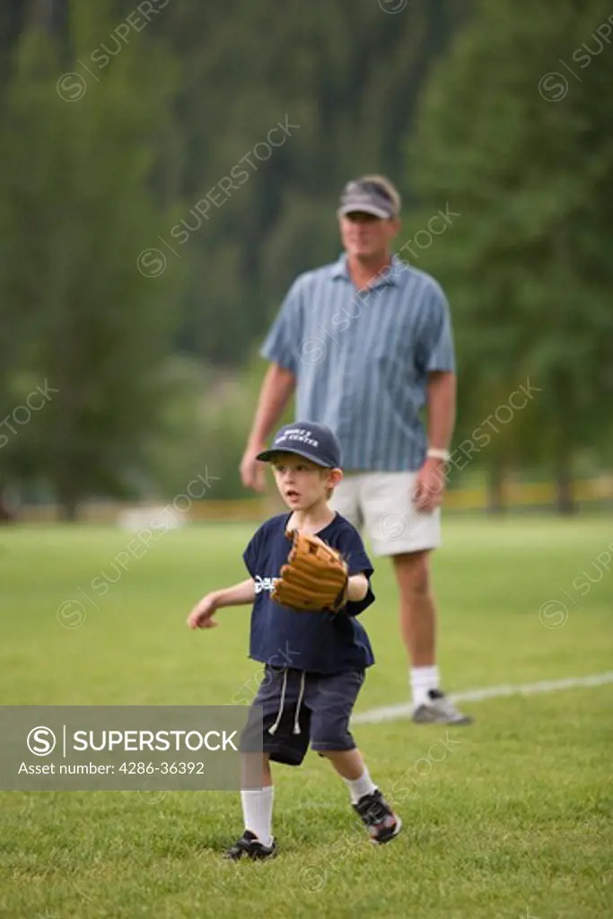 Young boy playing baseball with adult looking on behind him