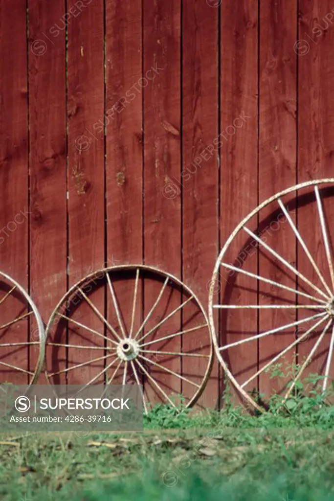 Wooden wagon wheels leaning against a red barn in western North Carolina.