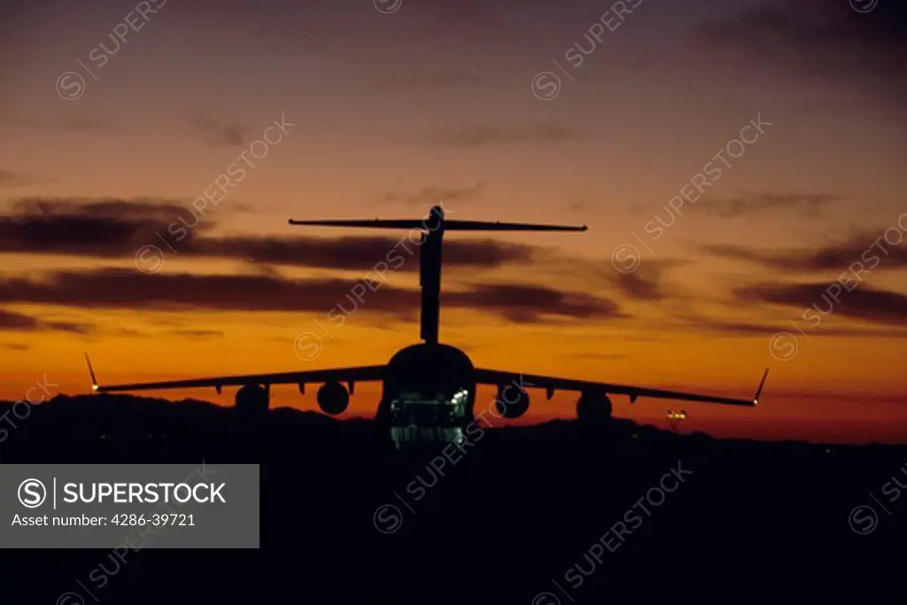 U.S. Air Force C-17 Globemaster III cargo plane silhouetted against the sky at sunrise.
