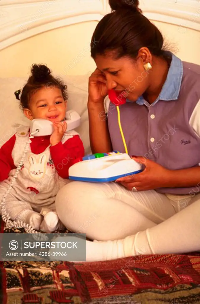 One-year-old African American girl playing telephone with her mother.