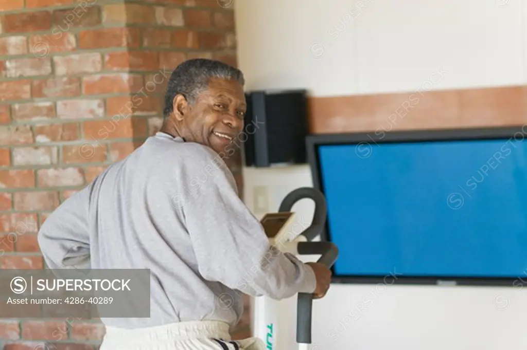 Senior, African American. Exercising on stepper machine and plasma TV  MR-0509 PR-0505