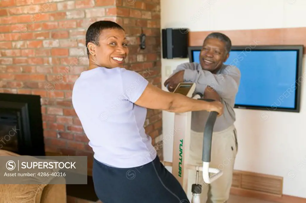 Seniors, African Americans. Exercising on stepper machine and plasma TV  MR-0509 MR-0510 PR-0505