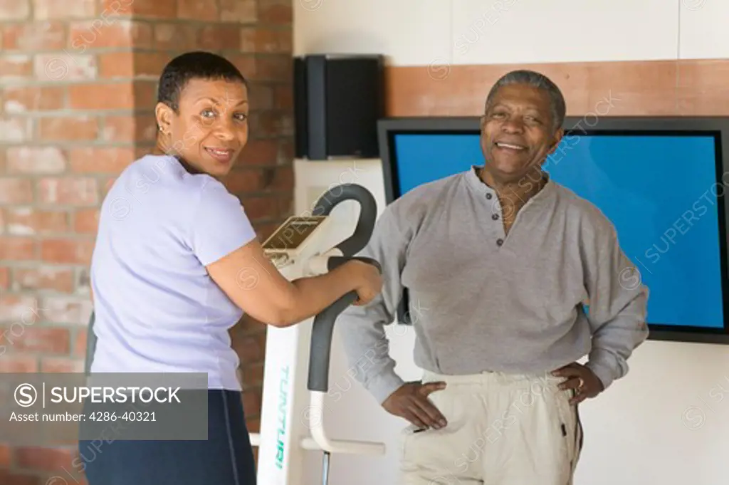 Seniors, African Americans. Exercising on stepper machine and plasma TV  MR-0509 MR-0510 PR-0505