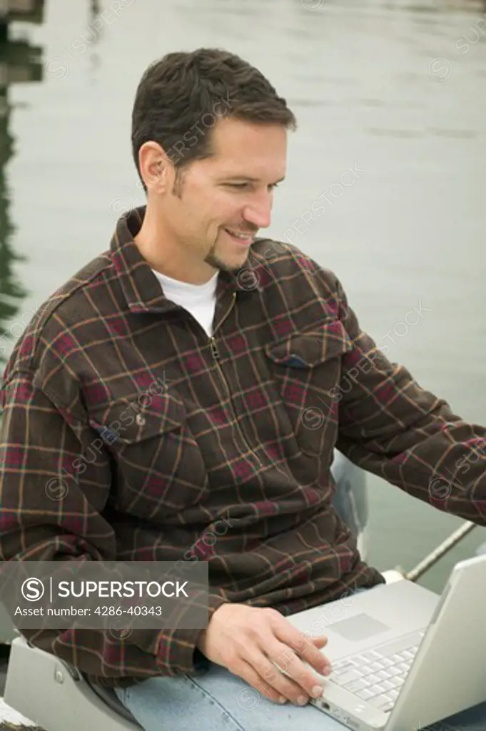 Man working on laptop in small boat.  MR-0422 PR-0424