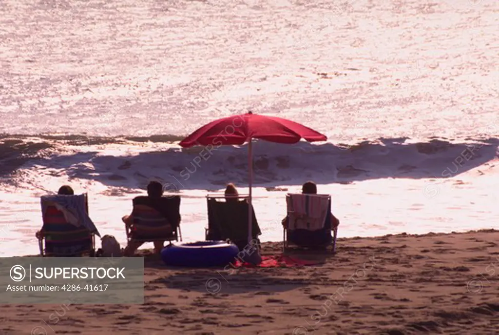 Four people sitting in beach chairs on the beach looking out at the surf, Rehobeth Beach, Delaware.