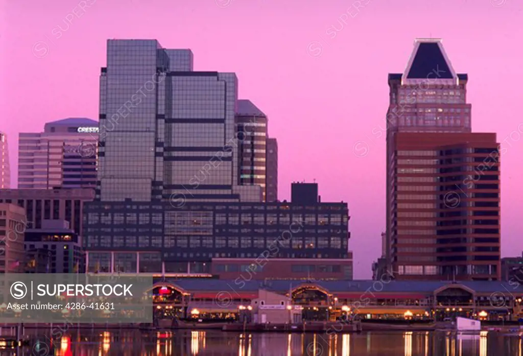Skyscrapers of Baltimore skyline with Inner Harbor market and Baltimore Harbor in the foreground at sunrise.