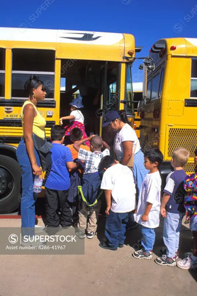 African American teacher supervises mixed ethnic elementary school children boarding school bus
