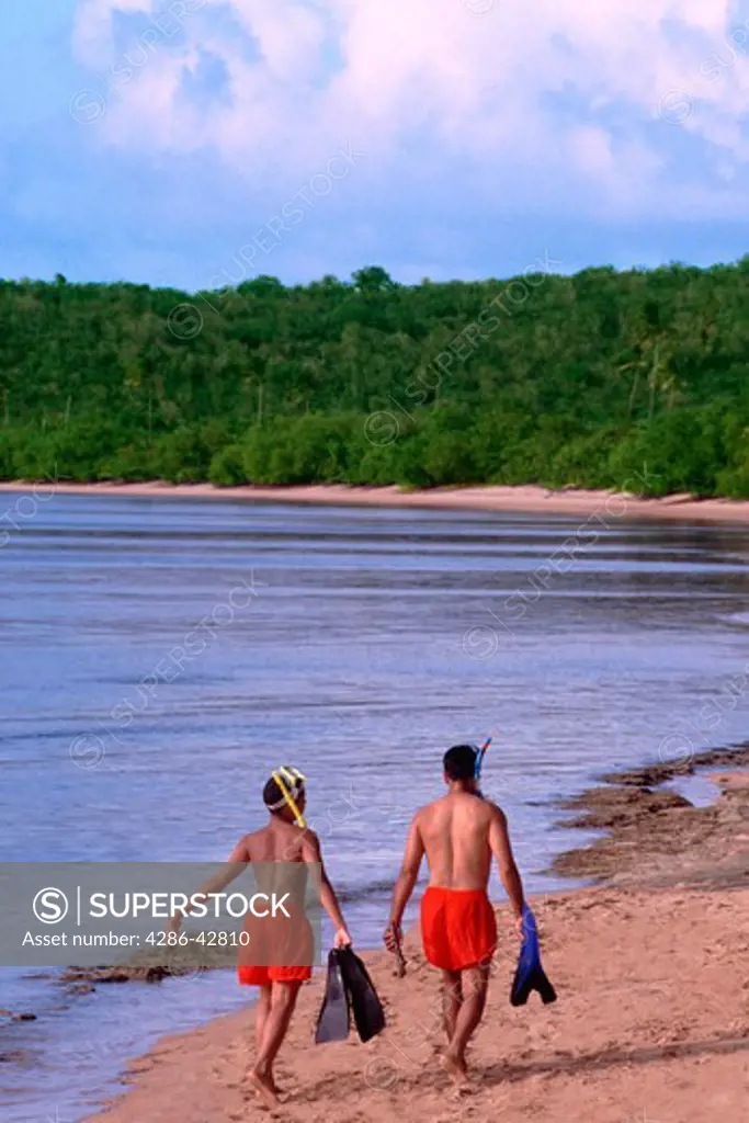 Two boys carrying snorkeling equipment along the beach.