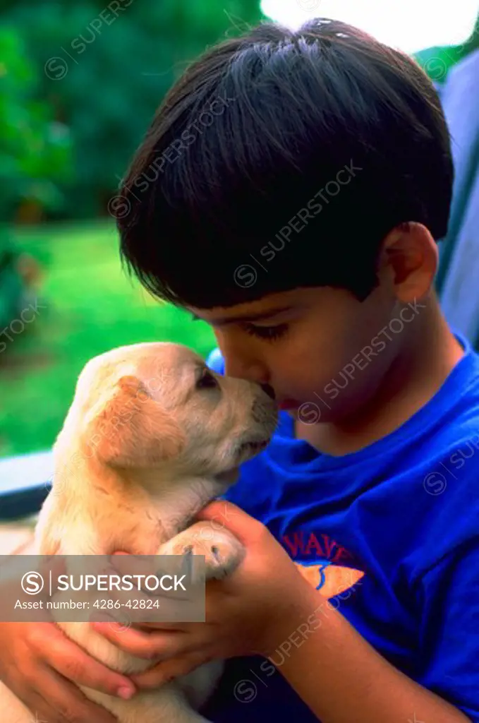 A young boy cuddling with a small blonde puppy.