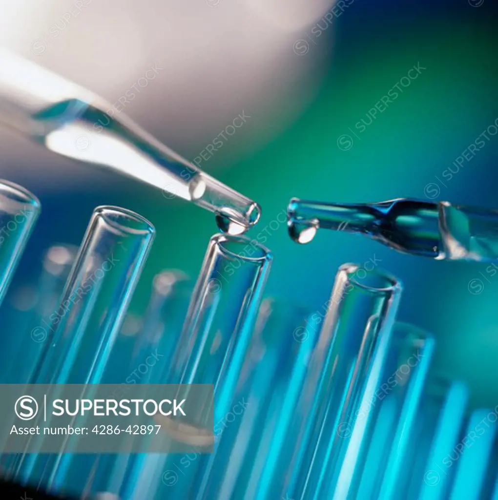 Close-up of a drop of clear liquid coming from each of two droppers and into one of a series of standing test tubes.