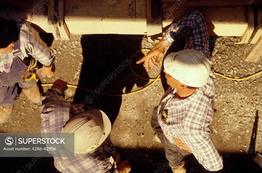 Overhead view of three hard-hat wearing construction workers talking at the work site.