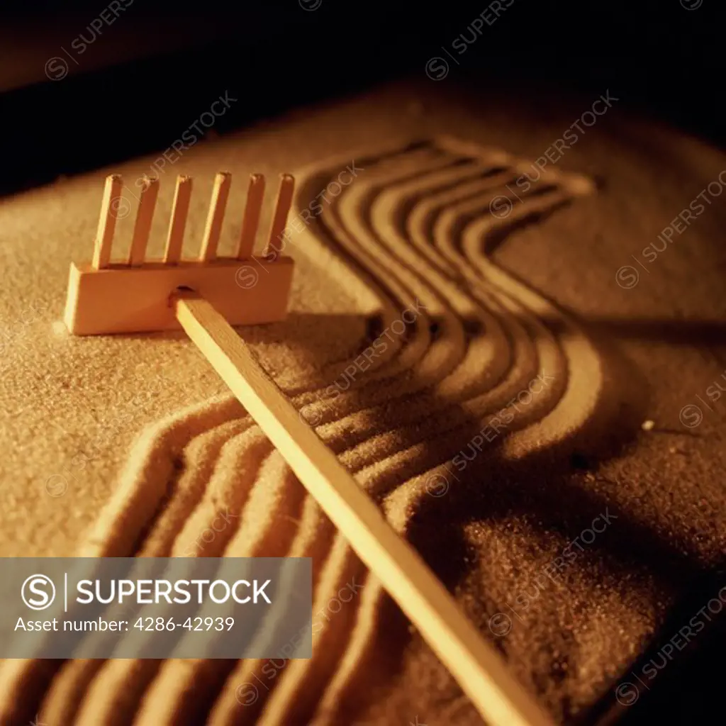 A miniature wooden rake lies across the patterns in a Zen sand garden.