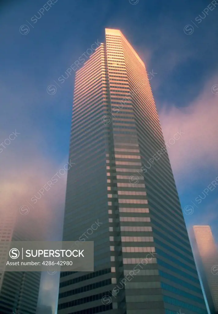 The Chevron Tower rises up through he clouds toward blue sky in Houston, Texas.