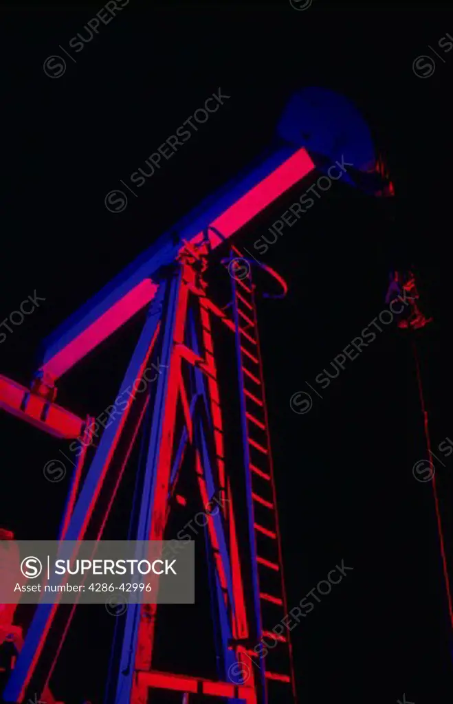View looking up at a pumpjack (oil pump) near Midland, Texas at night. The pump has been light painted so that it appears to be magenta and blue.