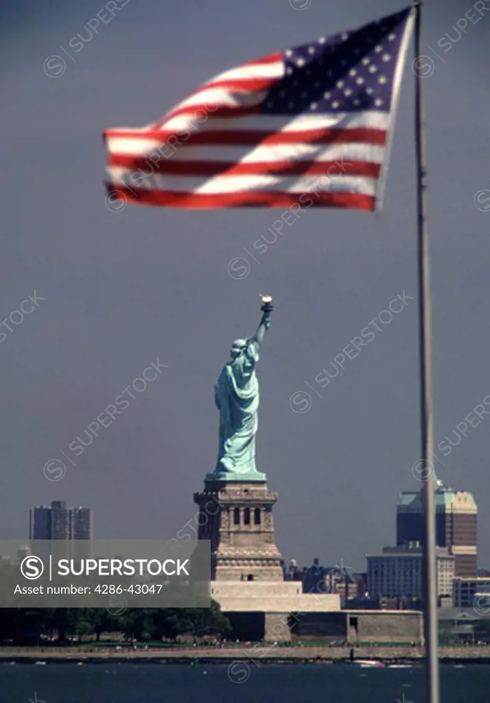The Statue of Liberty stands in the distance beneath a U.S. flag flying on the New Jersey shore.