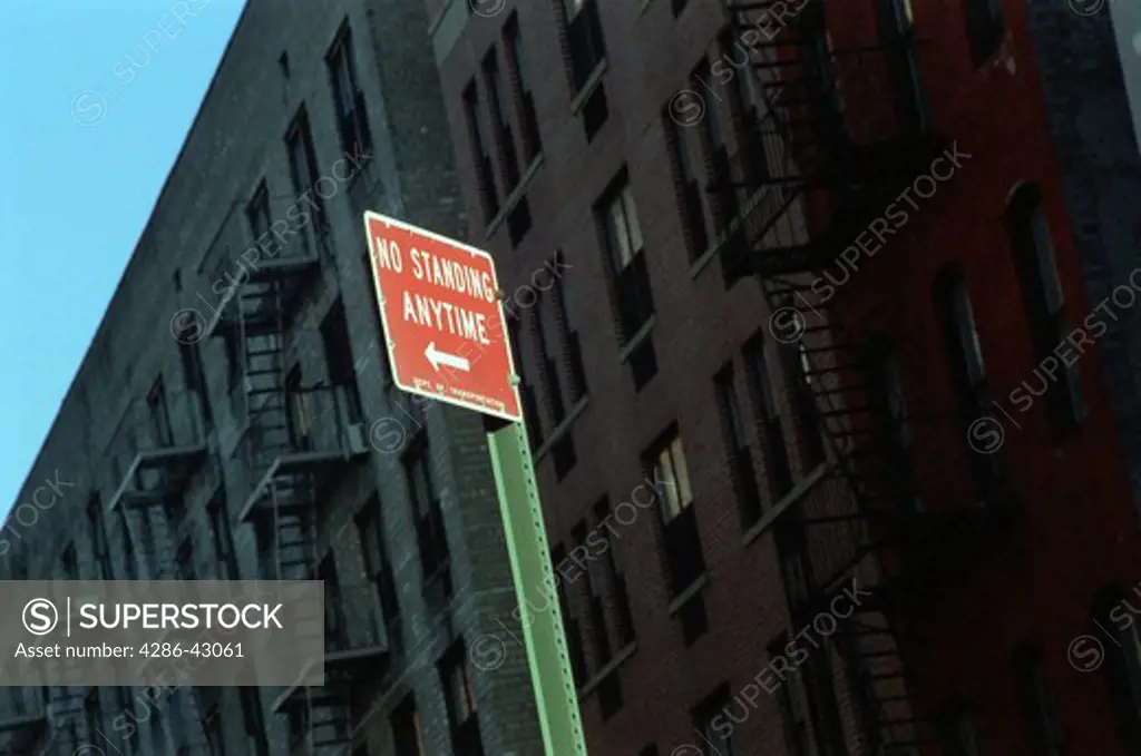 Close-up of a red 'no standing anytime' sign standing in front of a block of old dark stone apartment buildings in the city.