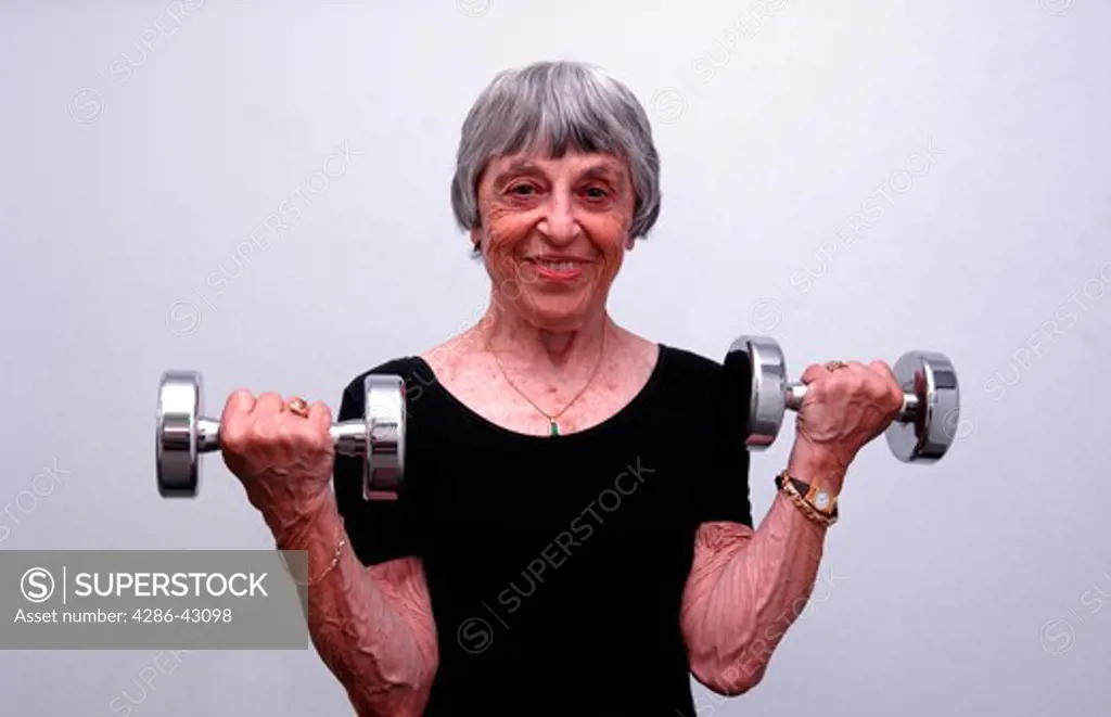Smiling senior woman in black leotard exercising with shiny metal hand weights.